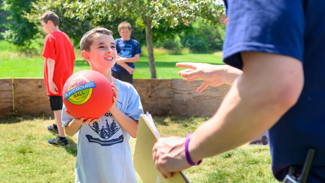 Camper with gaga ball smiling at staff